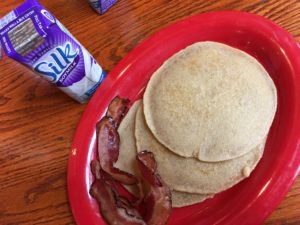 pancakes with bacon on a oval red plate and a small carton of soy milk on the side